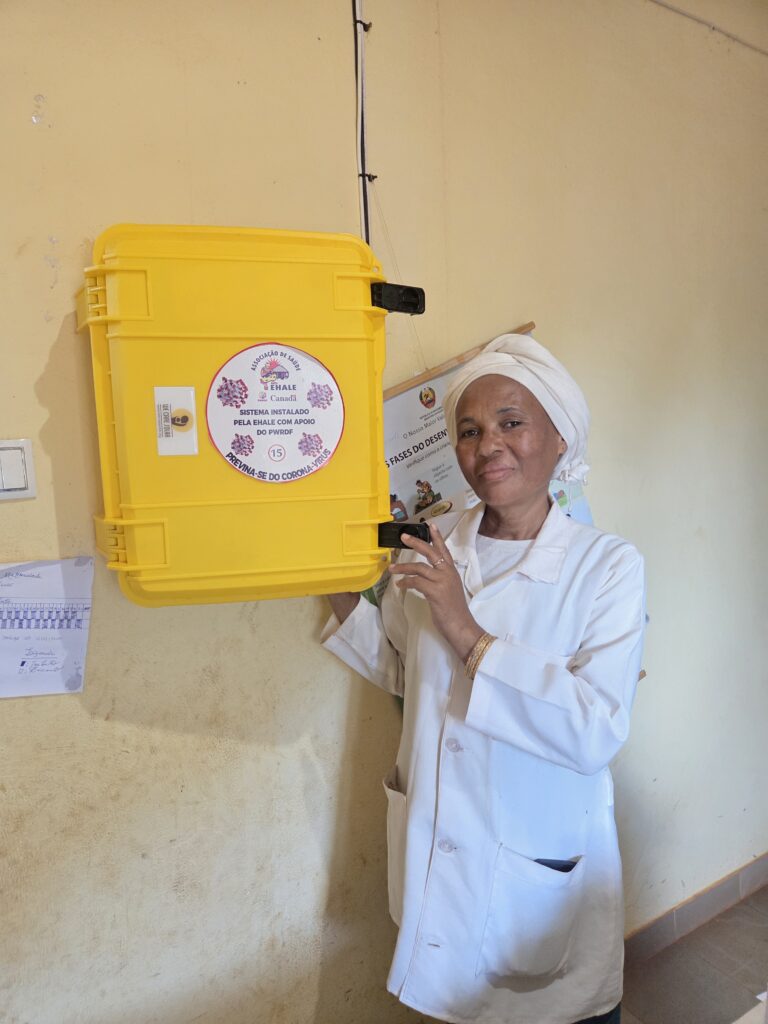 Healthcare worker in Mozambique stands beside a bright yellow Solar Suitcase installed by a Canadian charity to improve maternal care in remote clinics.