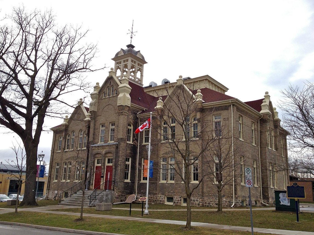 Historic brick building of the Aurora Cultural Centre in Ontario with a red roof and Canadian flag out front.