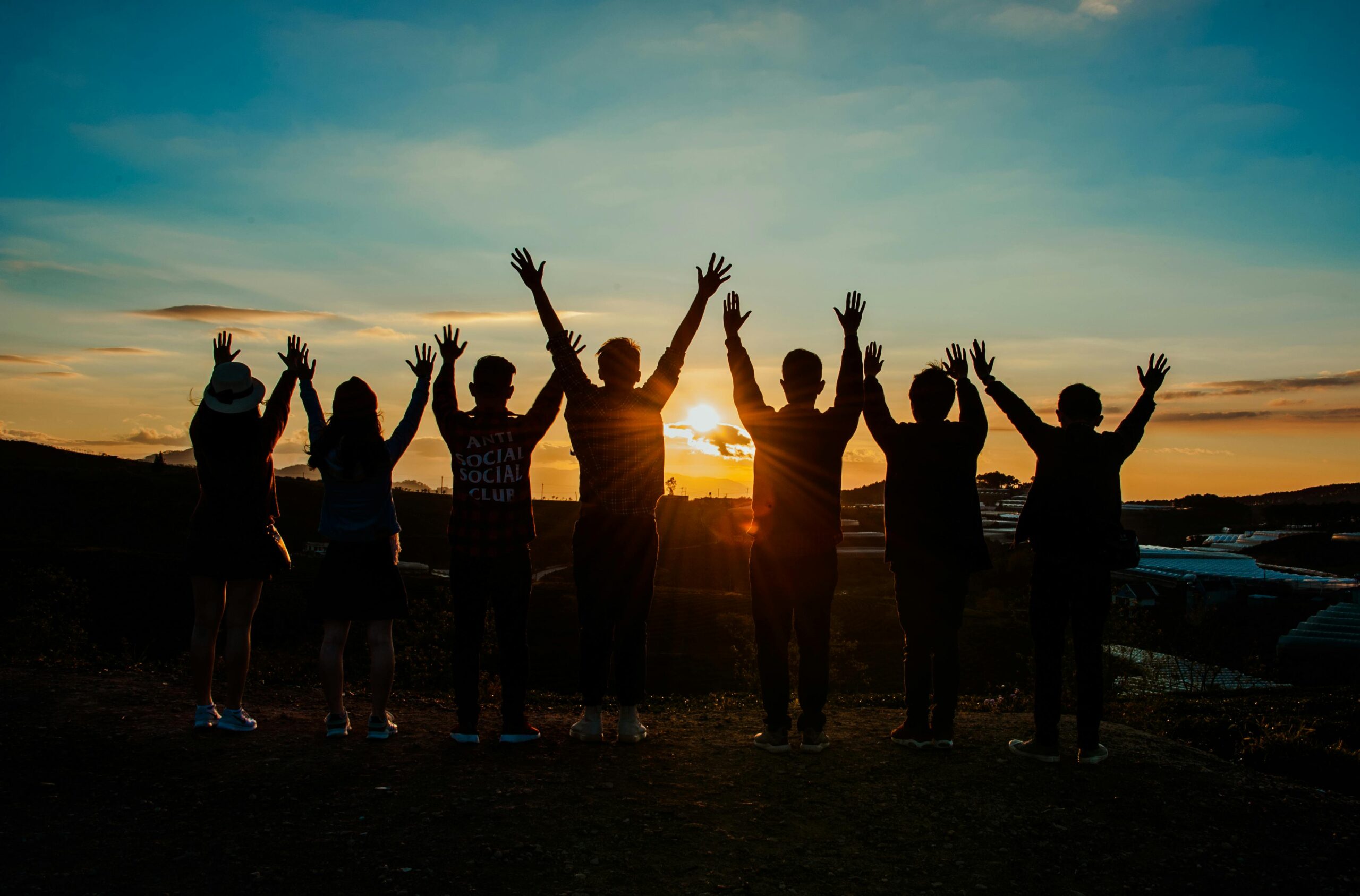 A team of people standing in unity with raised hands at sunset, symbolizing strength and community at the ALS Canada Pull to End ALS event.