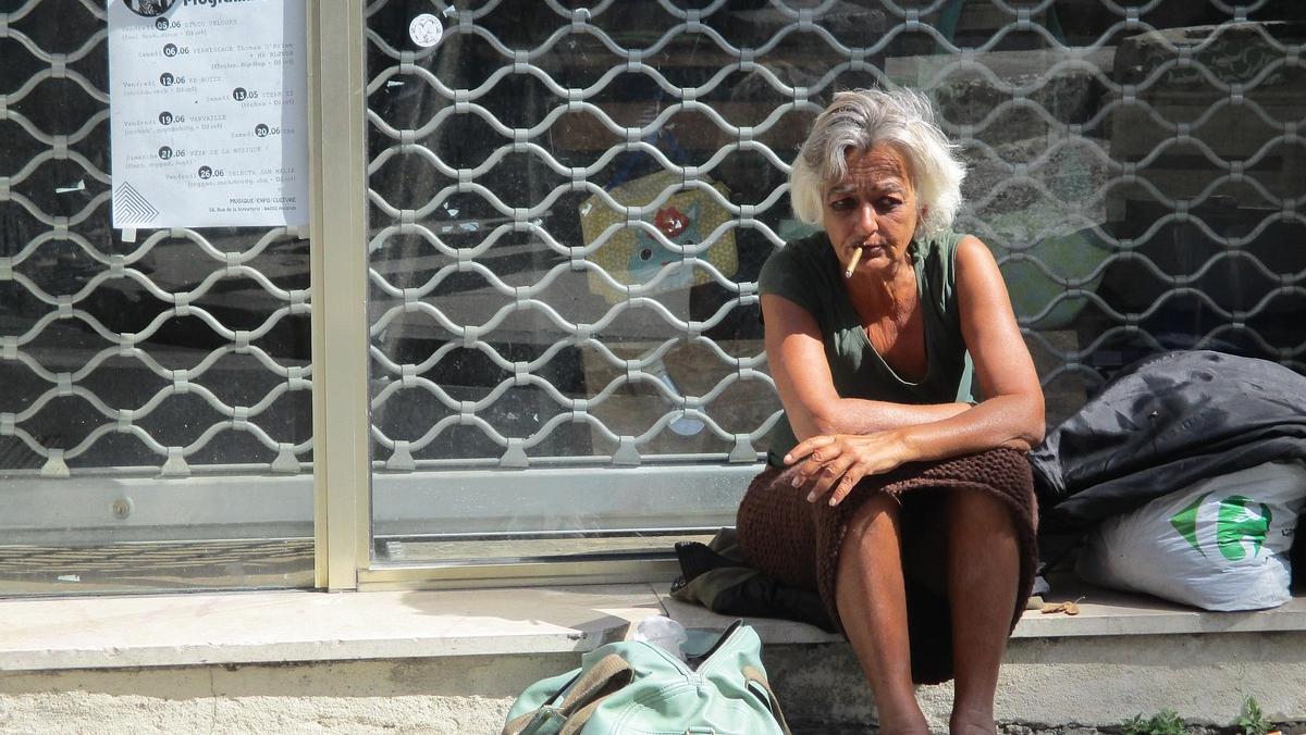Older woman sitting on a sidewalk with her belongings, illustrating homelessness and housing instability after hospital discharge.