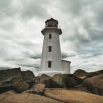 Lighthouse on a rocky shoreline in Nova Scotia under cloudy skies.
