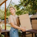 Single mother in a tan shirt and blue jeans carrying a moving box into a new apartment